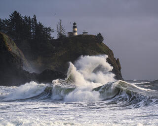 waves crashing at cape disappointment with north head lighthouse in the background on a hillside