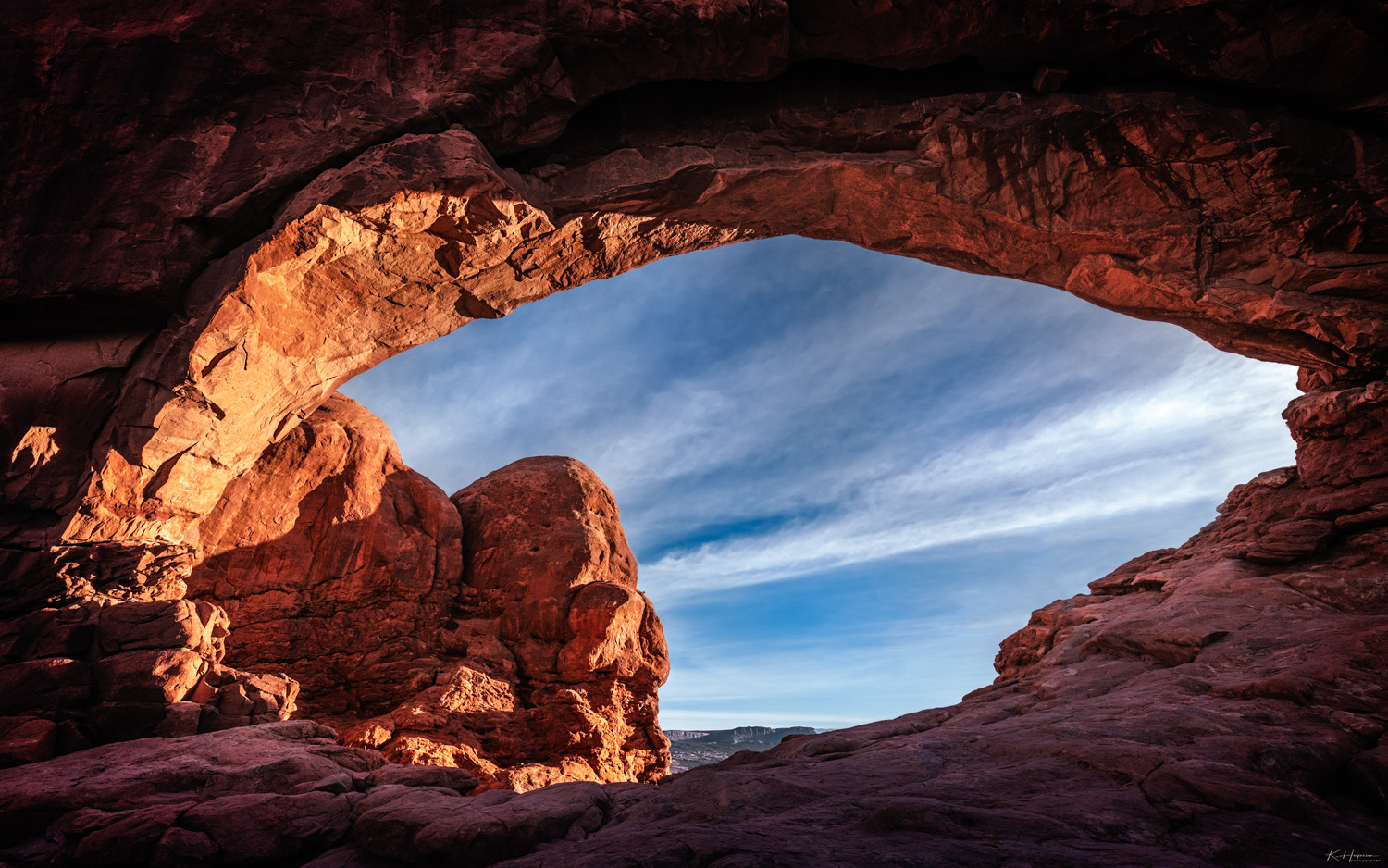 an arch in arches national park being illuminated by the morning sun with dark shadows on the leeward side and blue skies with white clouds in the background
