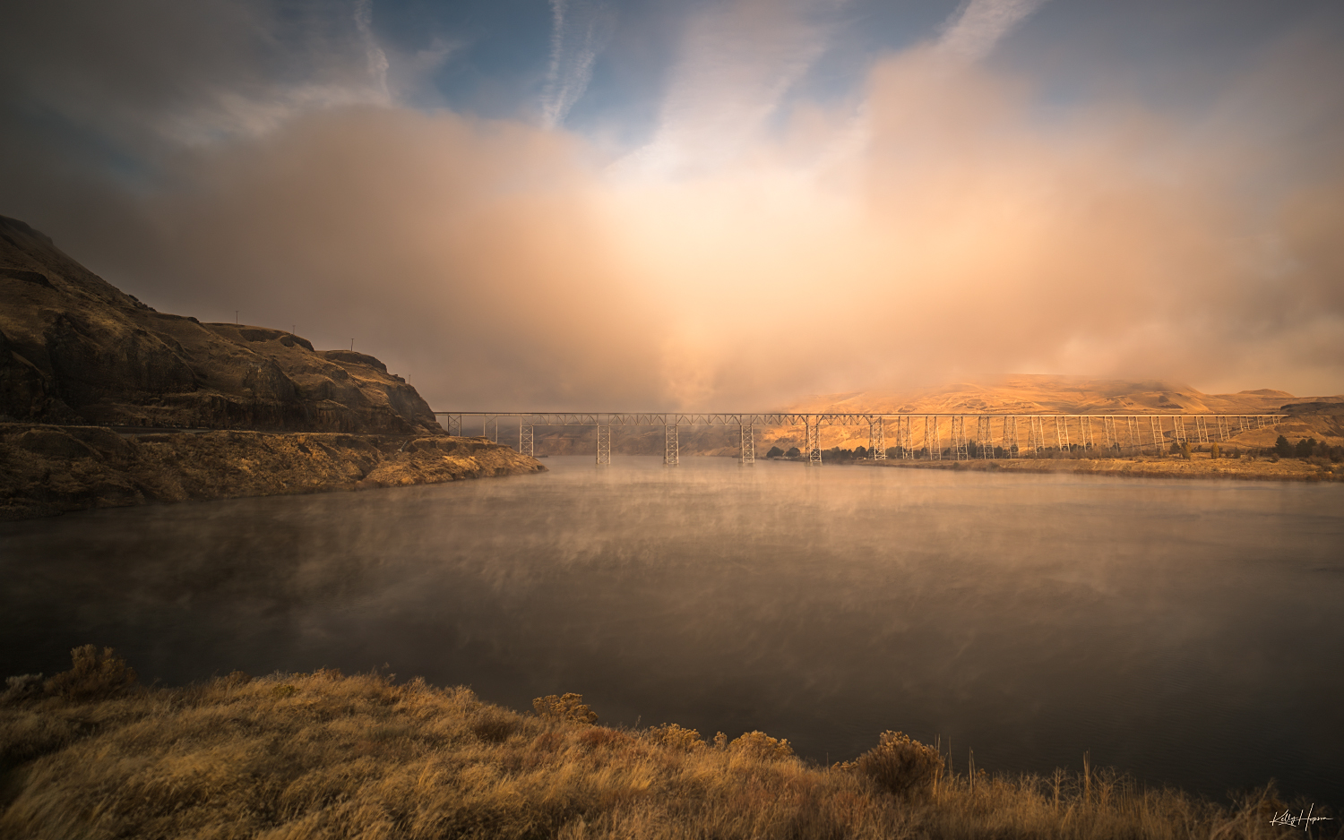 railroad bride over a river in desolate rocky high desert in south eastern Washington with stormy clouds in the sky and fog on the water