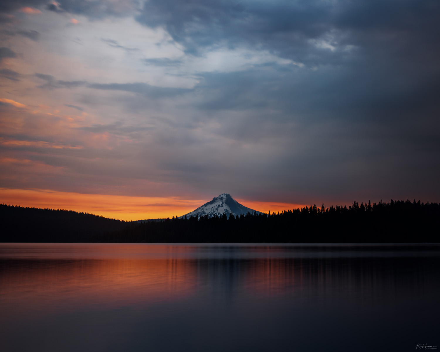 sunrise on timothy lake, mt. hood national forest. fiery glow from behind the mountain and reflecting on the water and dark forest in front of the mountain.
